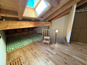 A loft bedroom with a skylight, wooden beams, a green patterned bed, and a small wooden stool. - High-end 4-room duplex at the foot of the slopes with parking (Les Adrets-Prapoutel)
