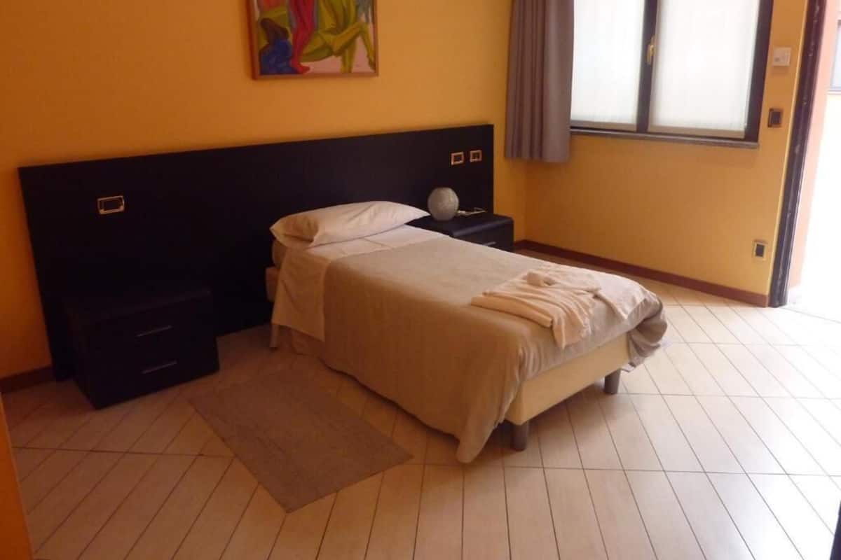 A bedroom with a bed, nightstands, a painting, and a window with curtains.