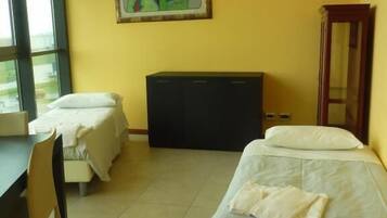Una camera d'albergo con due letti, una scrivania, una sedia, un'ampia finestra e un quadro appeso al muro.