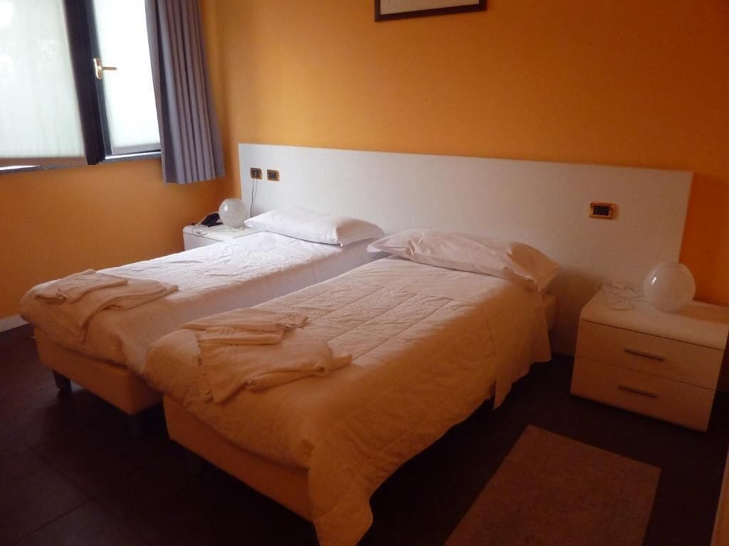 Un lit double avec du linge de lit blanc, une table de chevet avec une lampe et une petite table de nuit avec un téléphone.