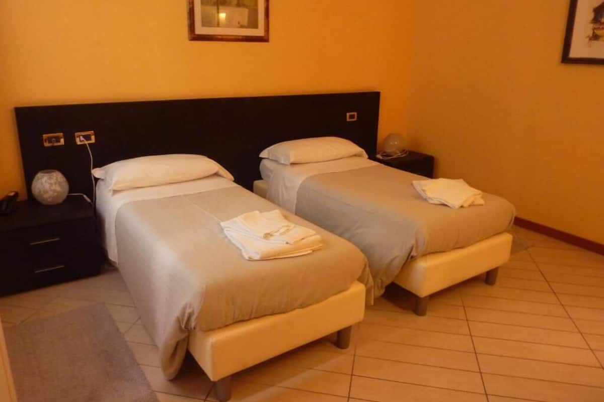 A hotel room with two beds, a nightstand with a lamp, and a framed picture on the wall.