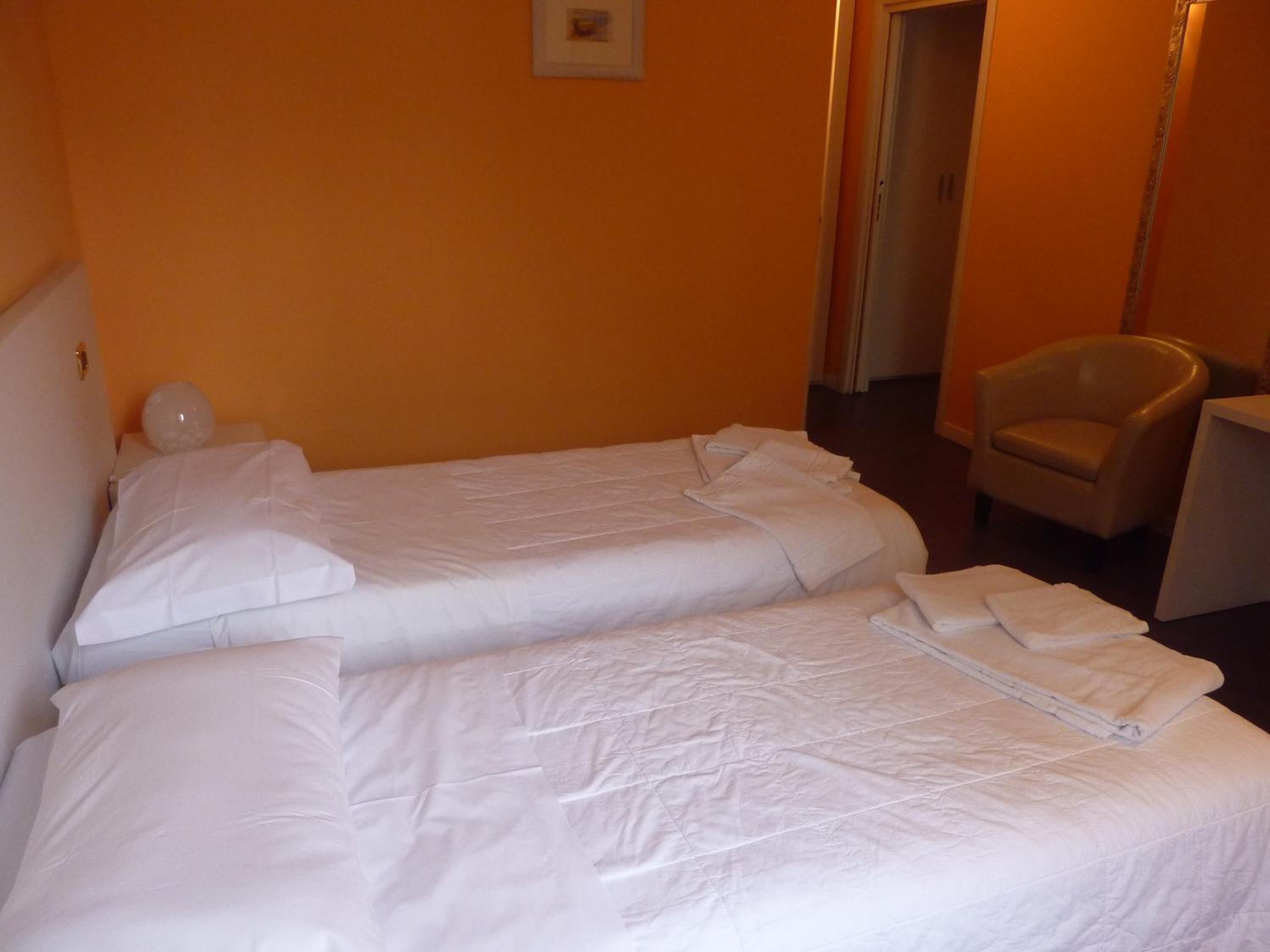 Camera d'albergo con due letti singoli, una sedia e una piccola scrivania.