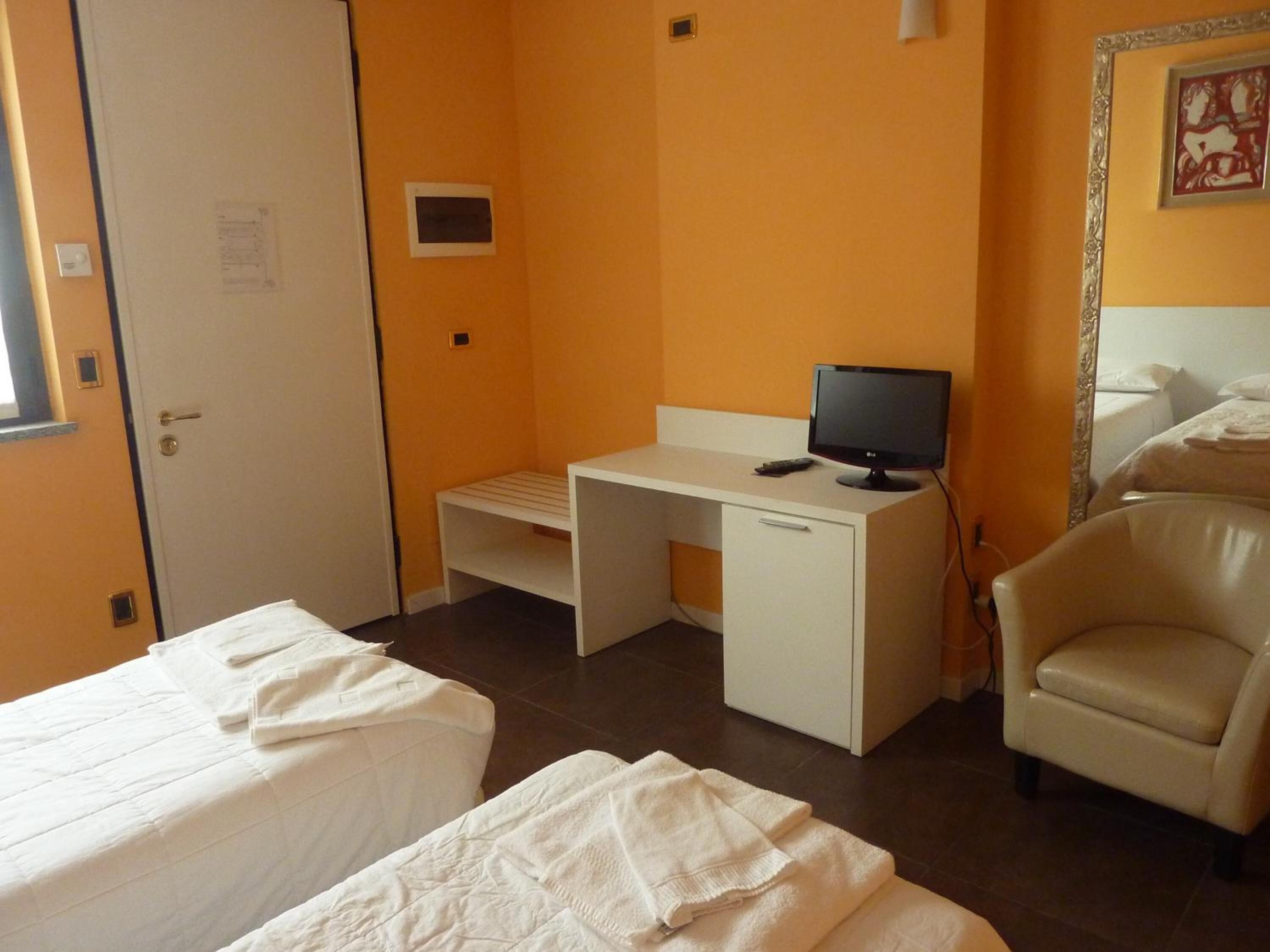 Ein Hotelzimmer mit zwei Betten, einem Schreibtisch mit Computer, einem Stuhl und einem Spiegel.