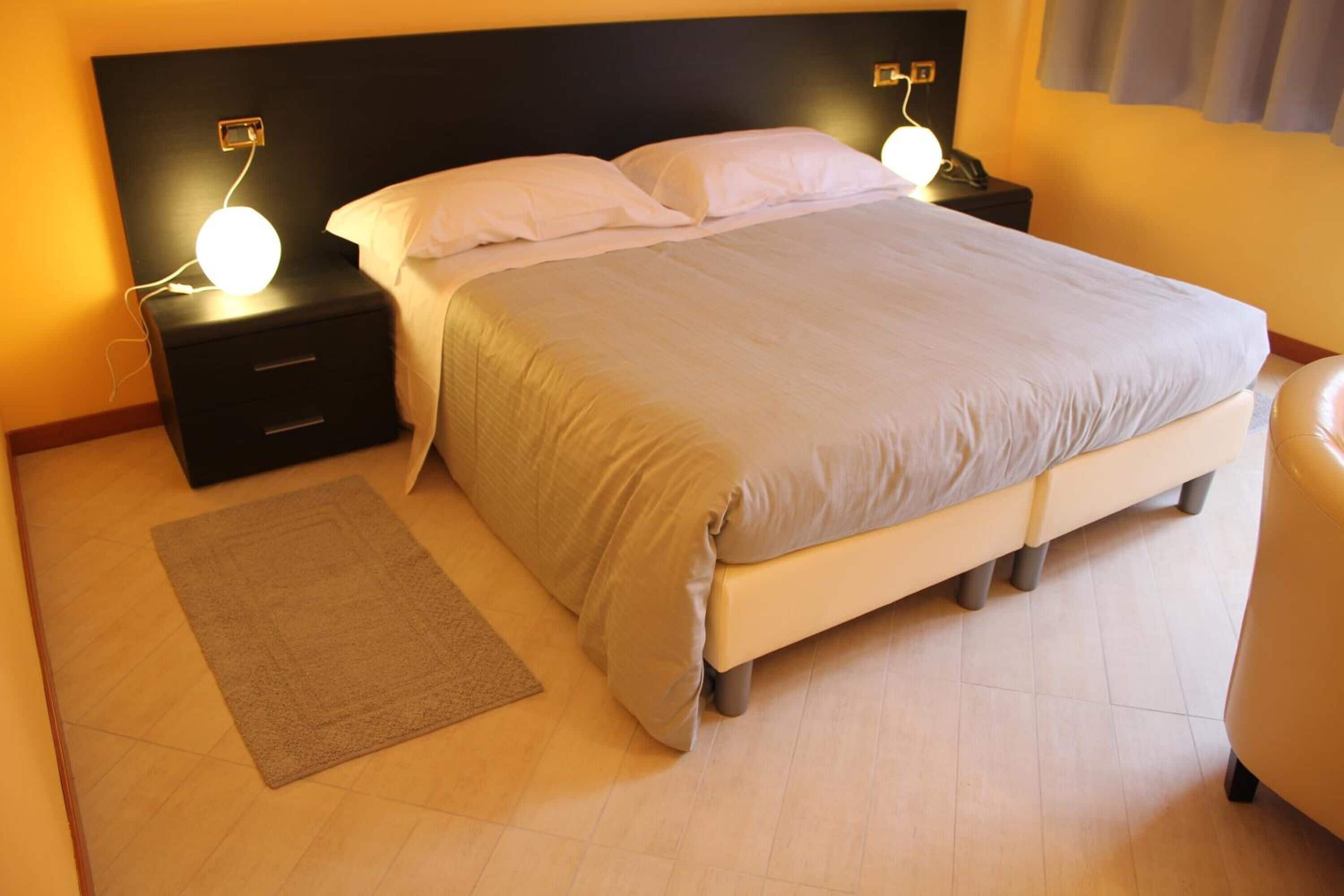 Una cama bien hecha con cabecera, mesitas de noche con lámparas y una alfombra sobre suelo de madera.