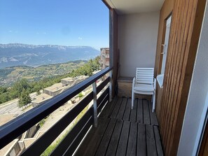 Uma varanda com piso de madeira e guarda-corpo de metal, com vista para uma paisagem montanhosa.