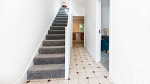 Un escalier dont les marches sont recouvertes de moquette mène à un palier, qui est lui-même doté d’un sol carrelé, et une porte donne accès à une pièce où se trouve une chaise bleue.