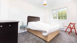 Une chambre à coucher avec un lit, une commode, une chaise, une lampe et une fenêtre.