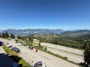 A parking area with vehicles, a small building, and a mountainous landscape in the background.