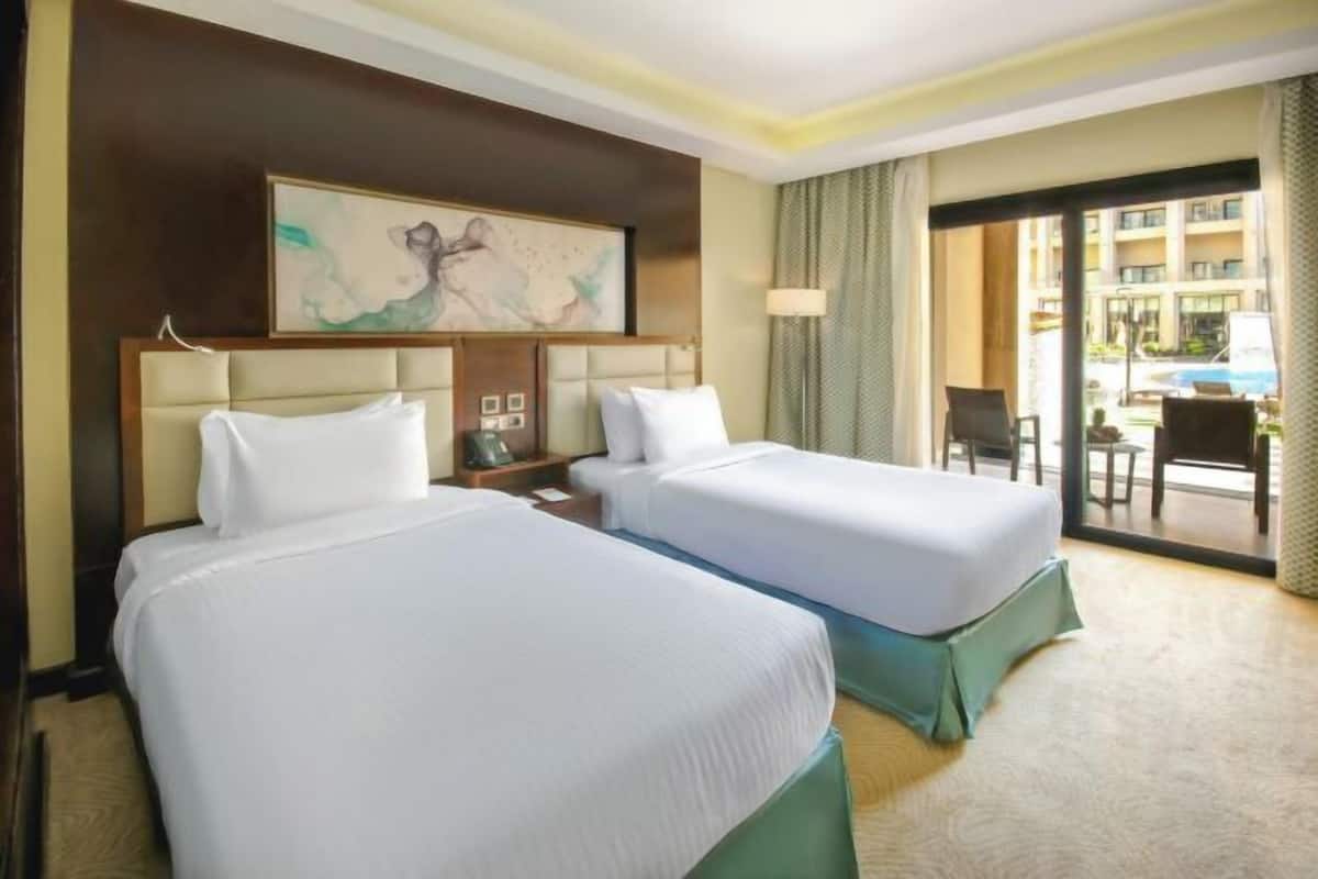 A hotel room with two beds, a large window, and a view of the pool and buildings outside.