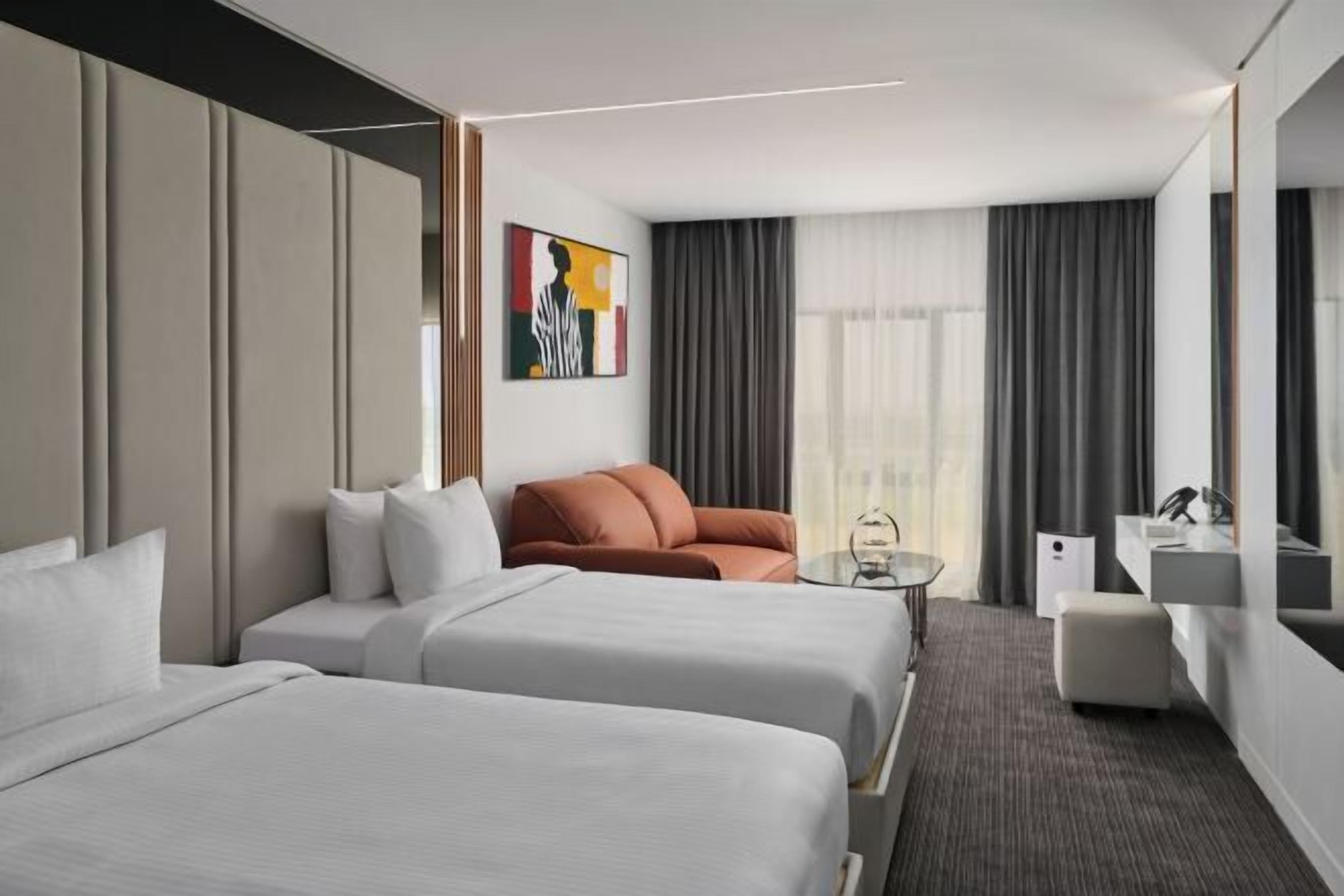 Habitación de hotel con dos camas, un sofá, una mesita, un espejo y una ventana con cortinas.