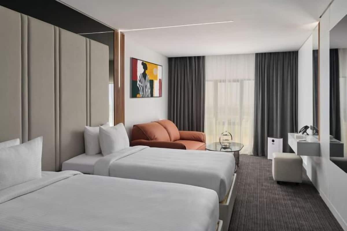 A hotel room with two beds, a sofa, a small table, a mirror, and a window with curtains.