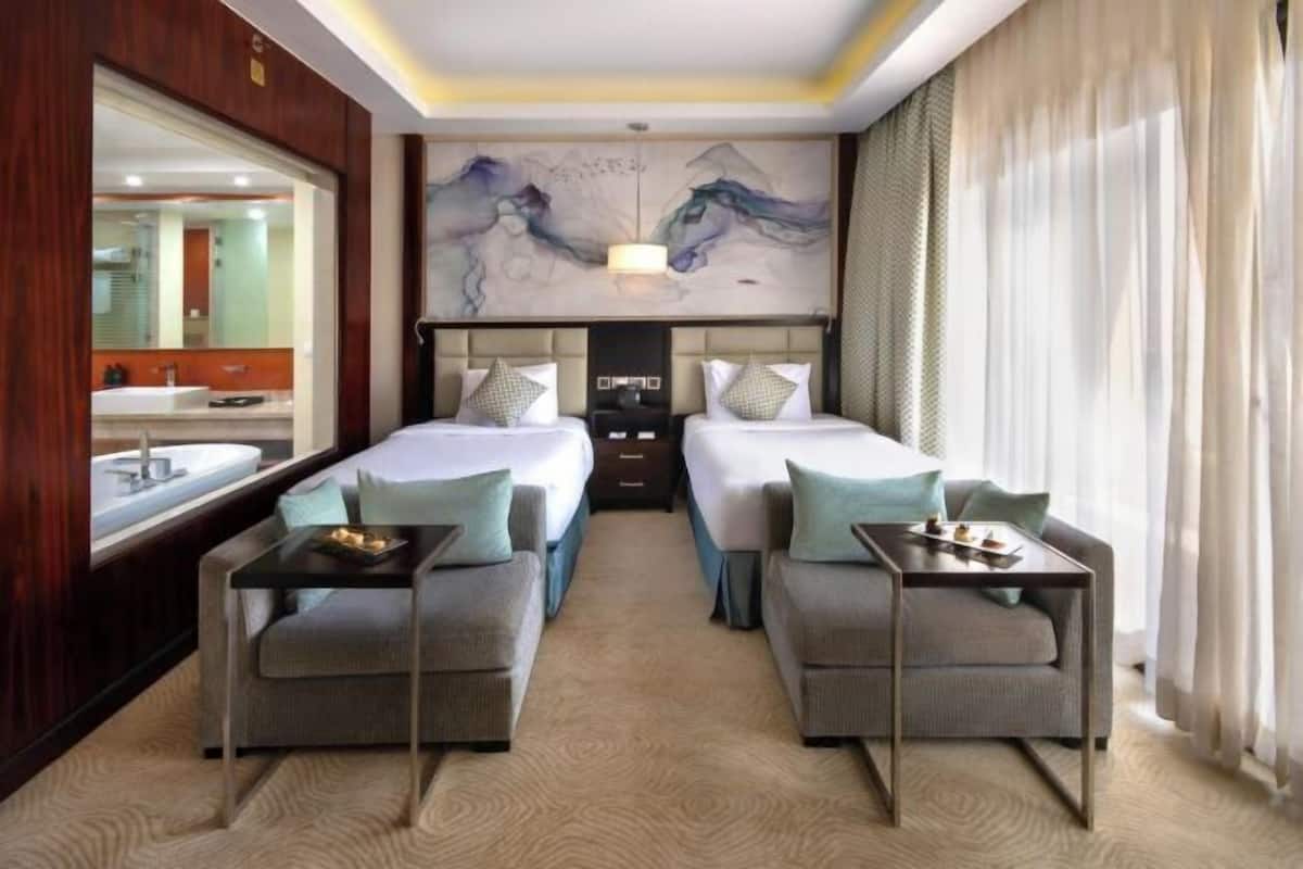 A hotel room with two beds, a sofa, a small table, a large mirror, and a painting on the wall.