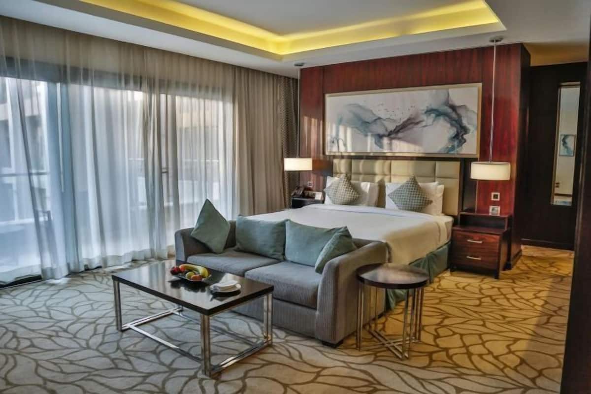 A hotel room with a bed, a sofa, a small table, a lamp, and a painting on the wall.