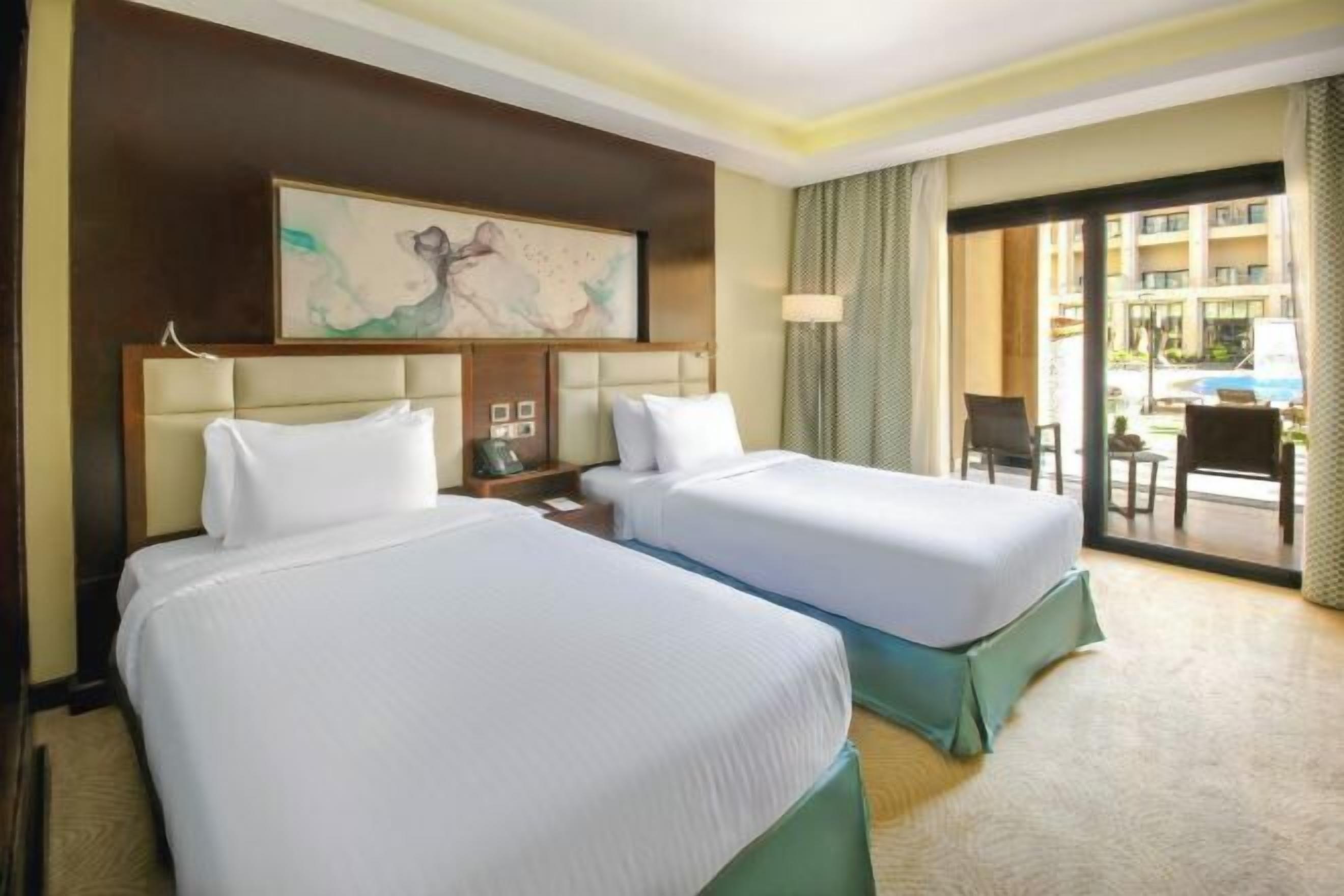 Habitación de hotel con dos camas, un ventanal grande, un cuadro en la pared y vistas al exterior.