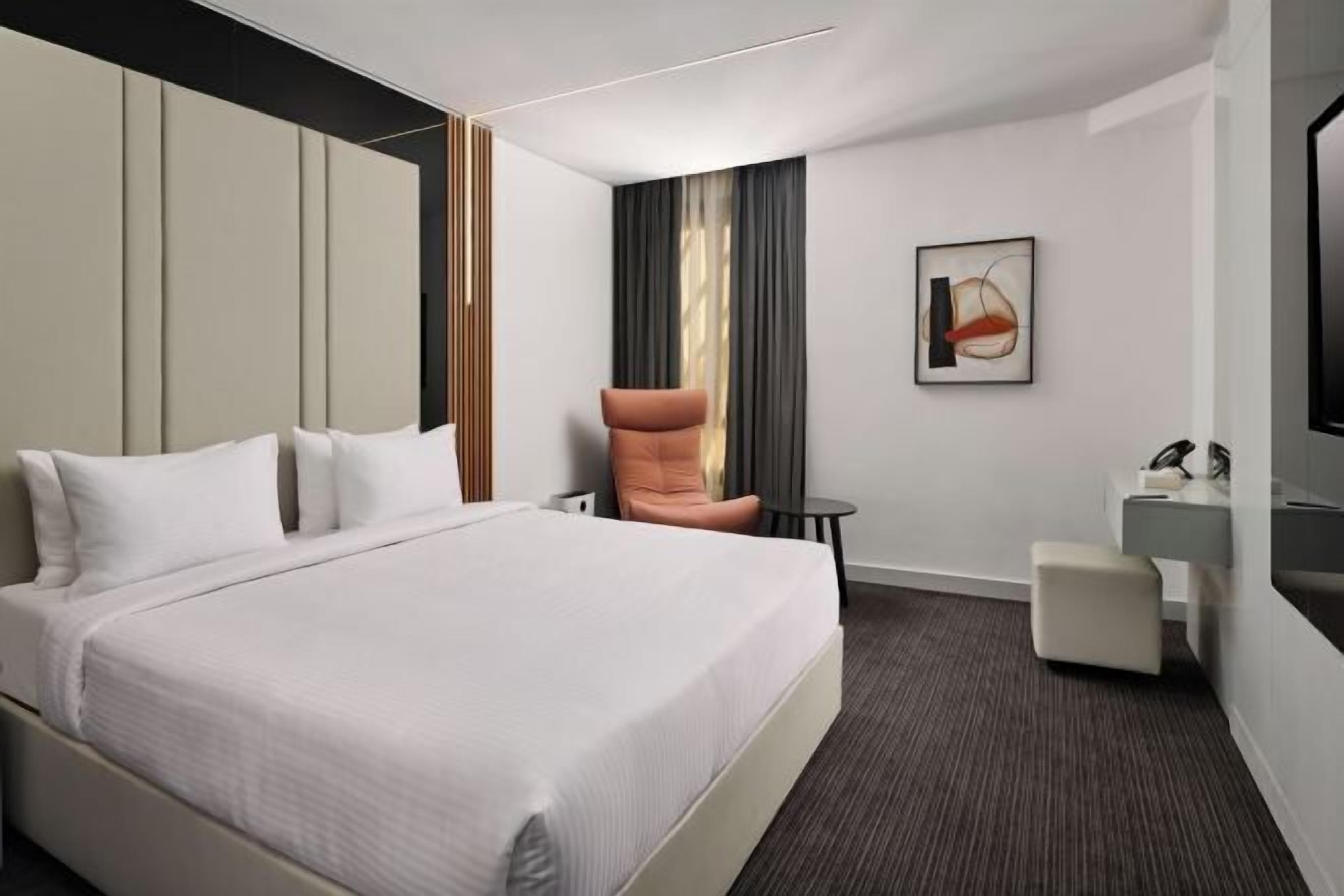 Una habitación de hotel moderna con una cama grande, una zona de estar, una mesita y un televisor.