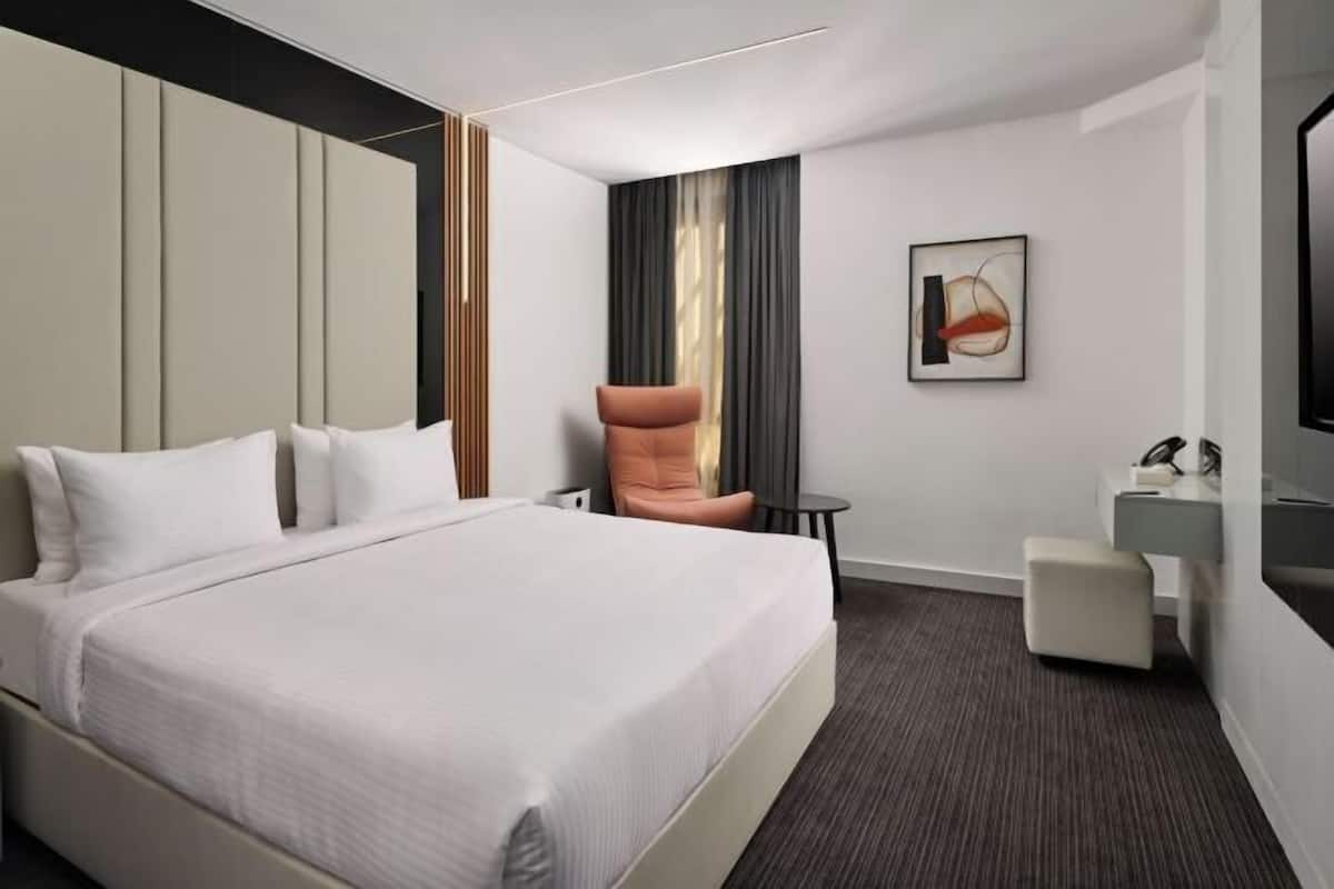 A modern hotel room with a large bed, a seating area, a small table, and a TV.