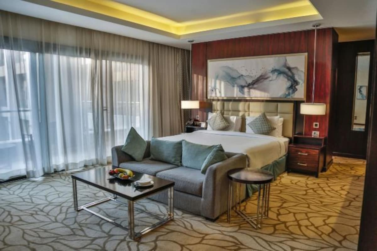 A hotel room with a bed, a sofa, a small table, a lamp, and a painting on the wall.