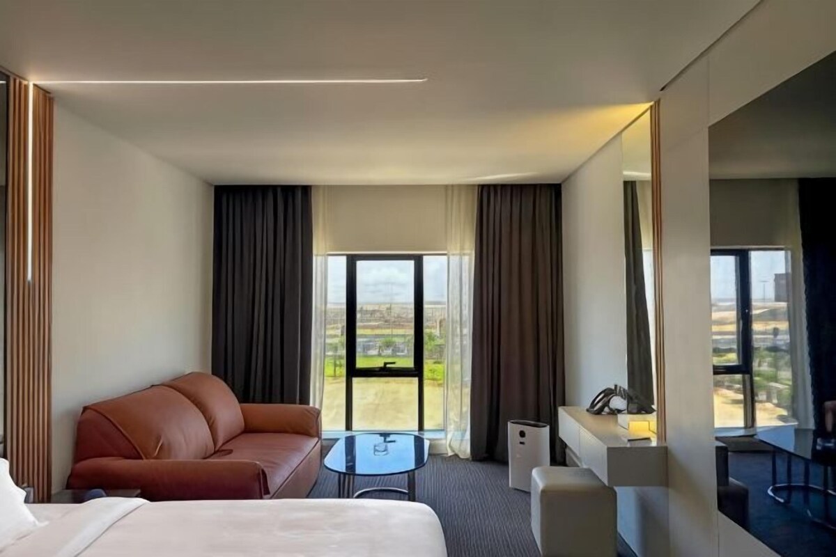 A hotel room with a bed, a sofa, a small table, a chair, and a view of the outdoors.