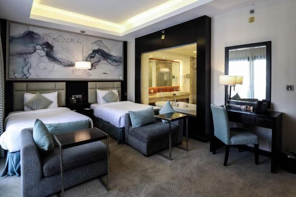 A hotel room with two beds, a desk, a chair, and a large abstract painting on the wall.