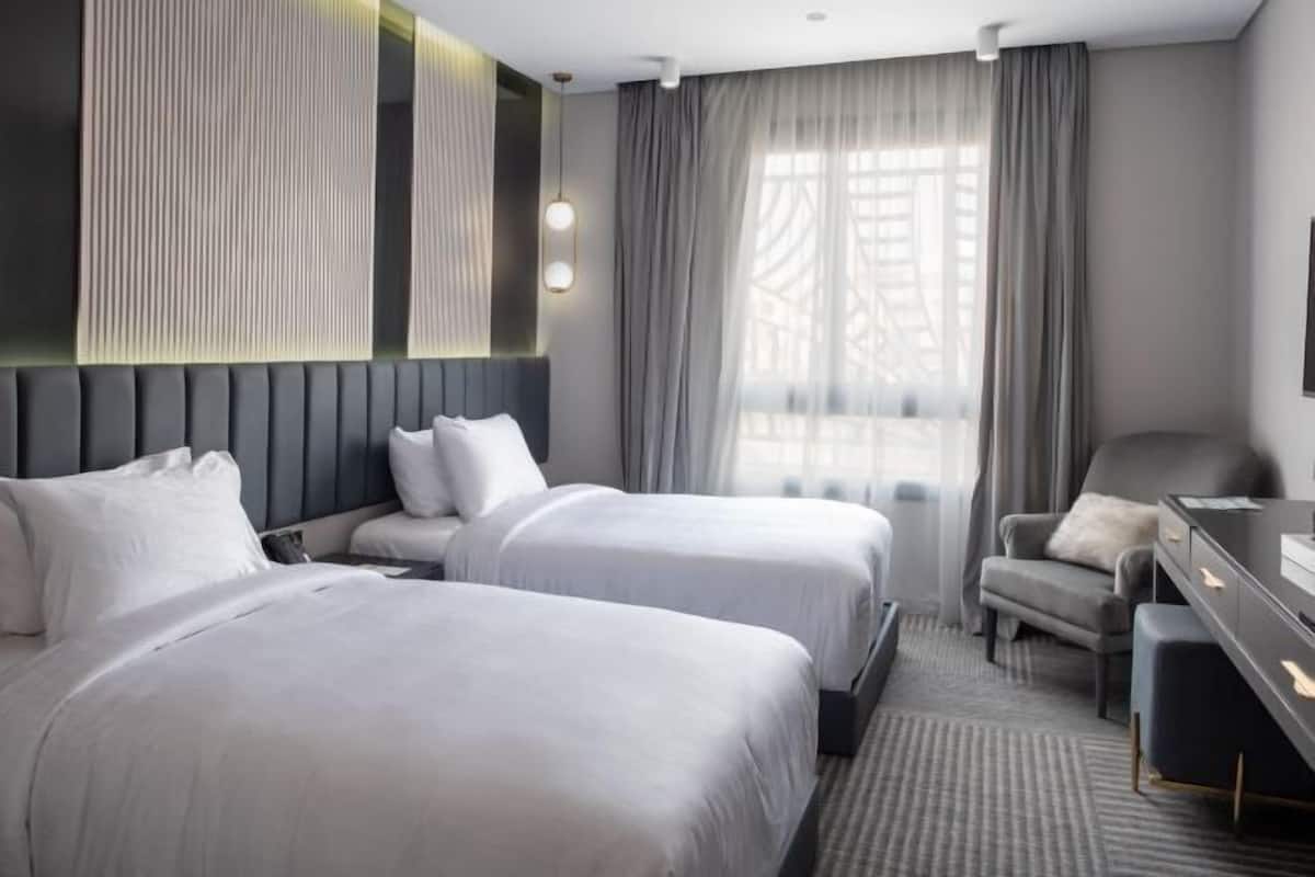 A hotel room with two beds, a desk, a chair, and a large window with curtains.