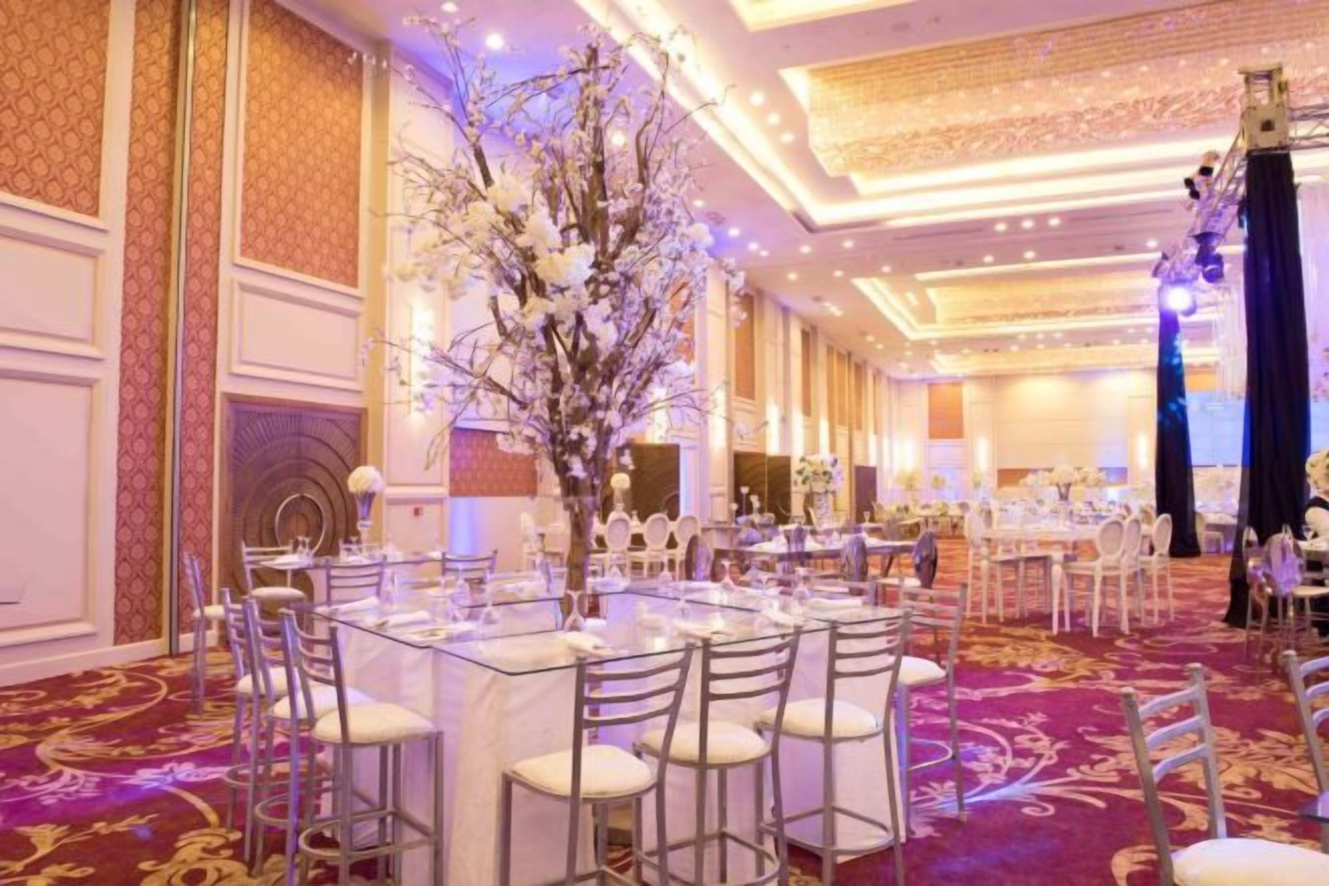 Un salón de banquetes con mesas redondas, sillas y un arreglo floral central.