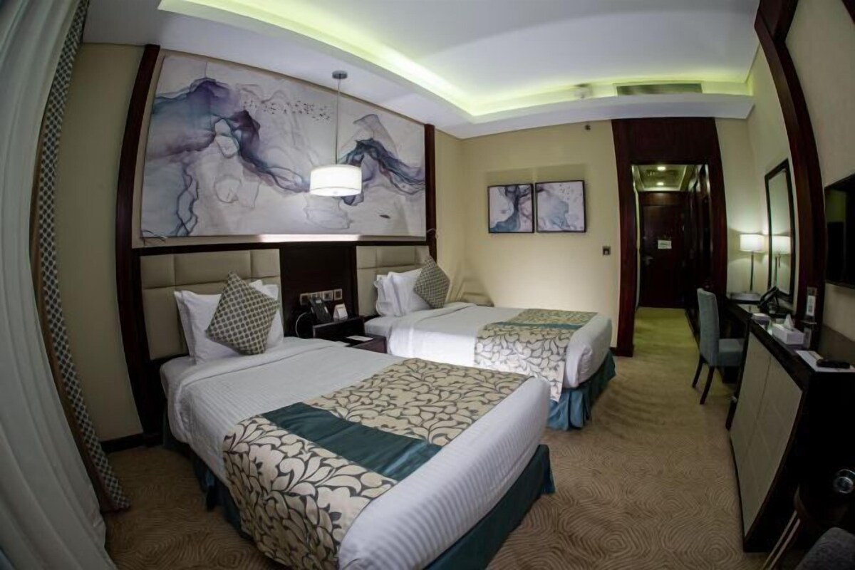 A hotel room with two beds, a large abstract painting on the wall, a desk with a computer, and a mirror.