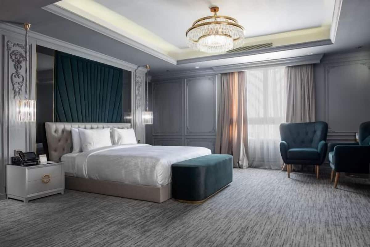 A modern hotel room with a large bed, a nightstand, a chair, and a chandelier.