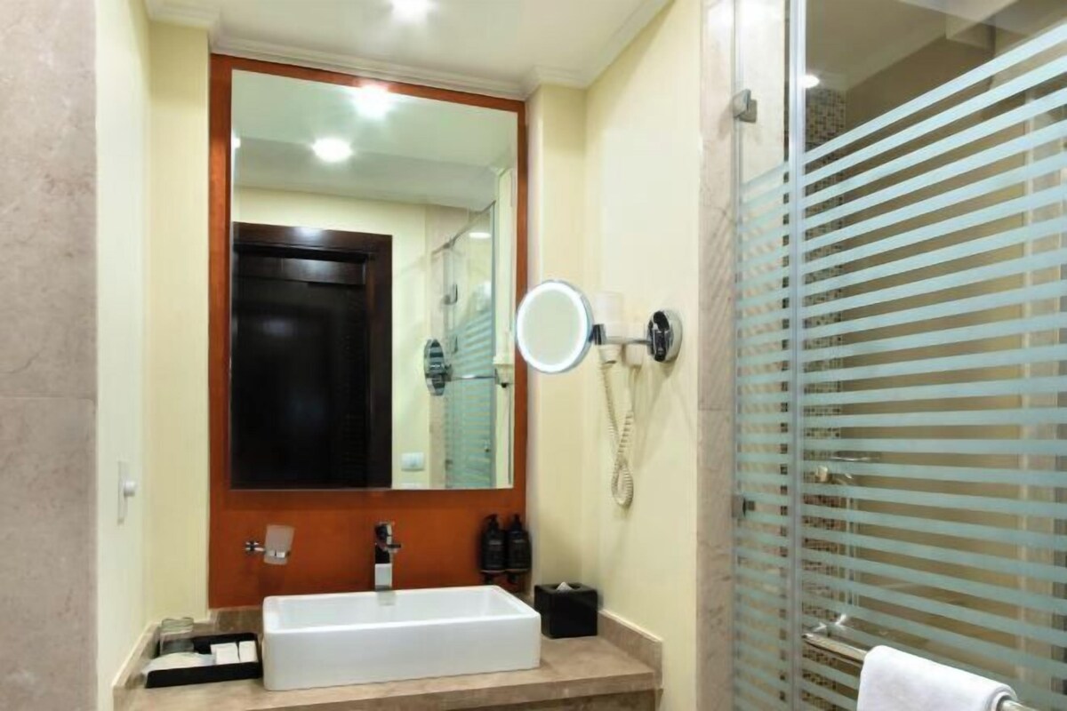 A bathroom with a rectangular sink, a mirror, a telephone, and a shower area with frosted glass doors.