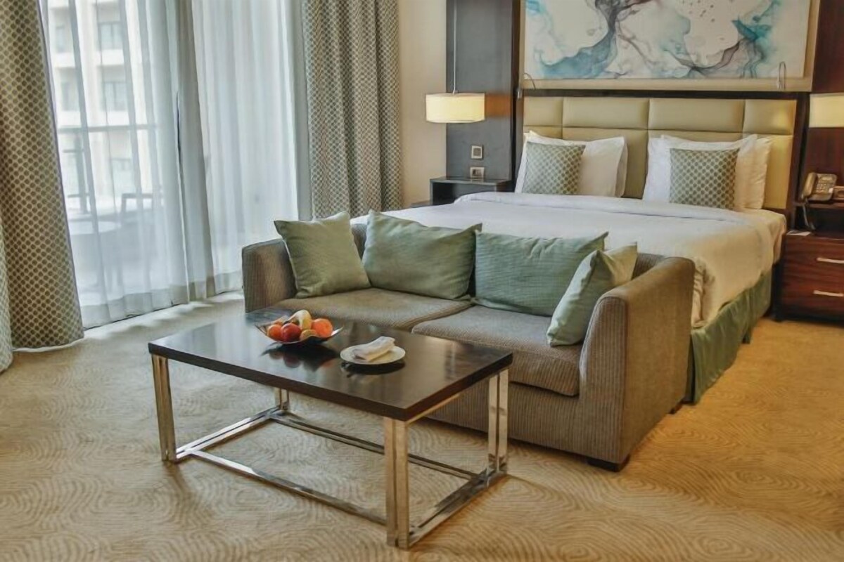 A hotel room with a bed, a sofa, a small table, and a painting on the wall.