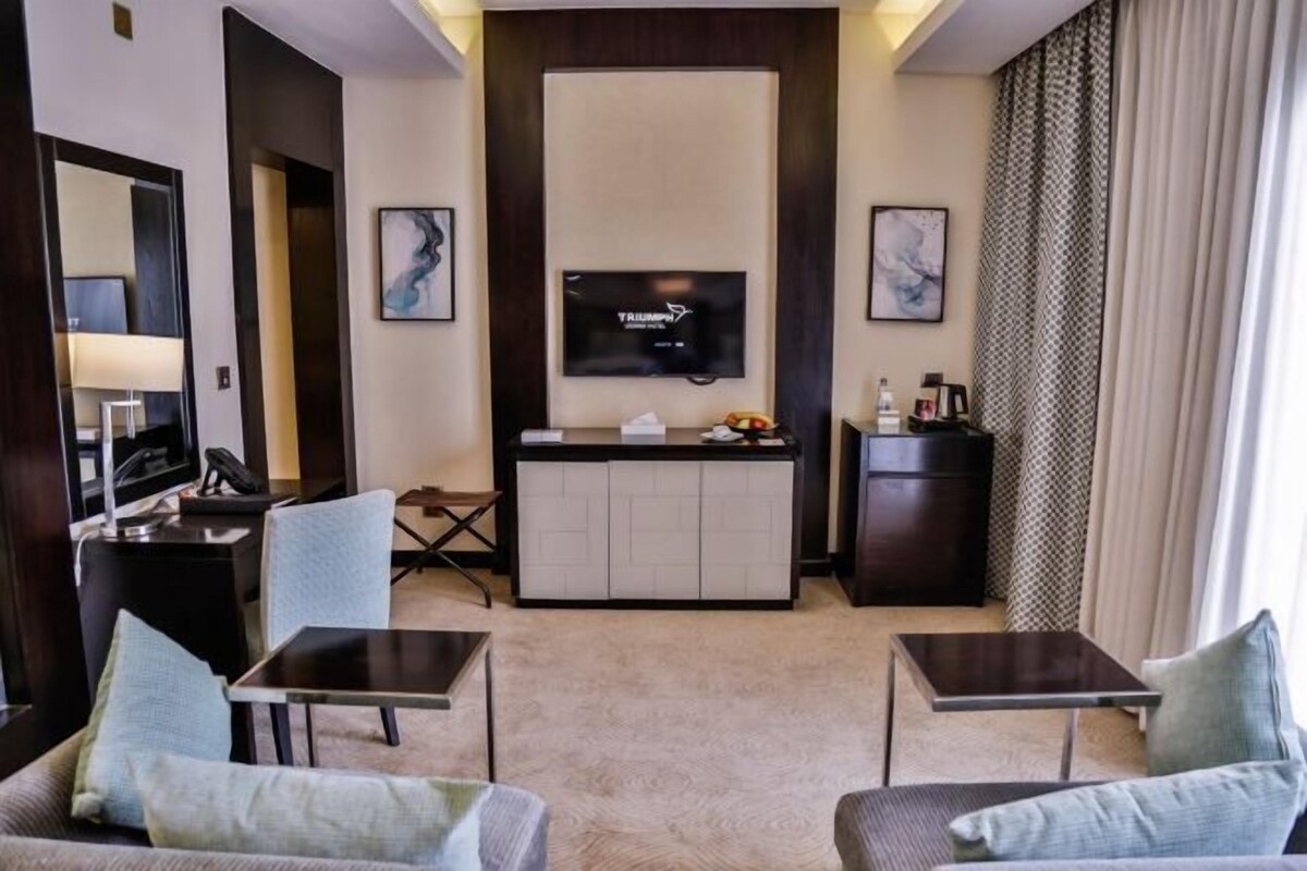 A hotel room with a TV, a desk, two chairs, a sofa, and a minibar.