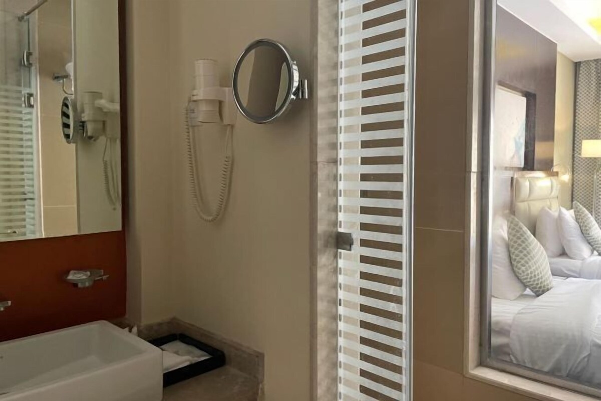 A hotel bathroom with a bathtub, a mirror, a hairdryer, and a shower.