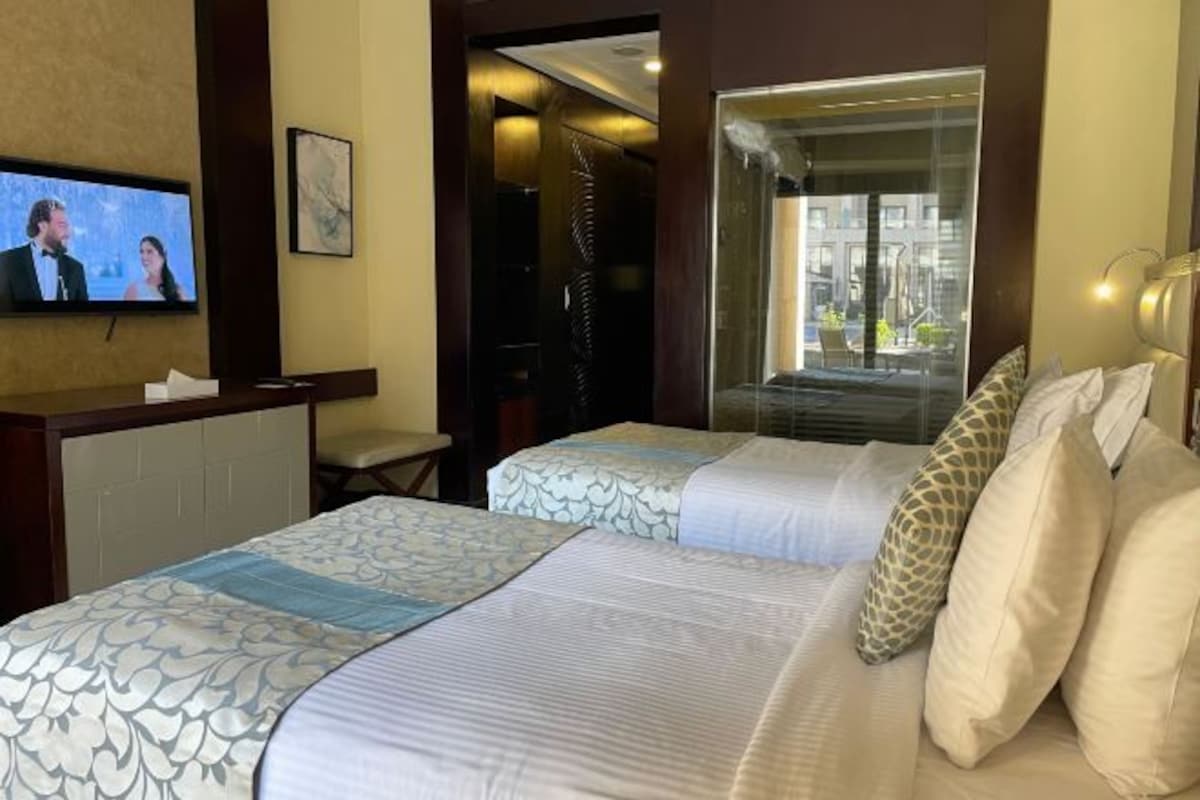 A hotel room with two beds, a TV on the wall, a window with a view, and a door leading to a bathroom.