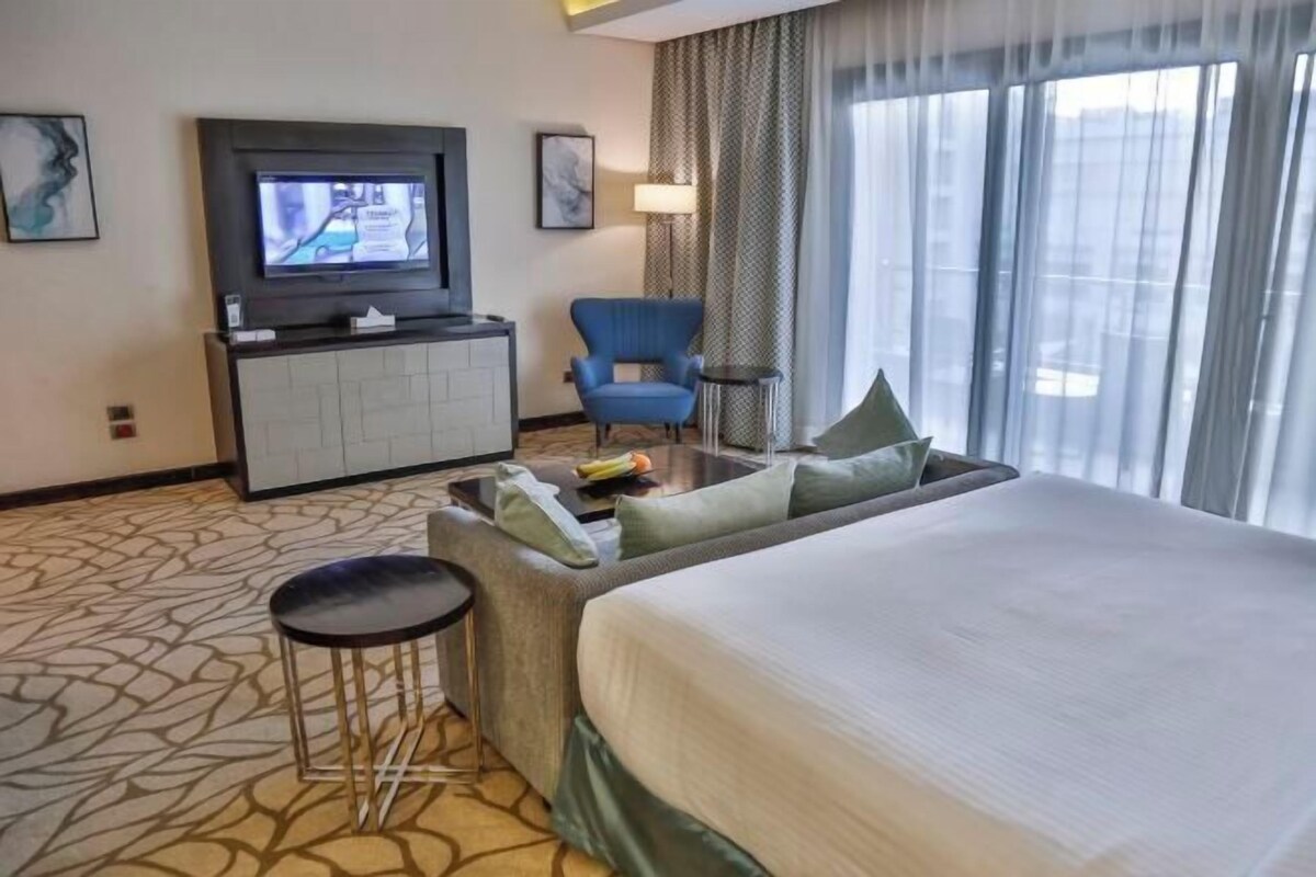 A hotel room with a bed, a sofa, a TV, a desk, and a chair.