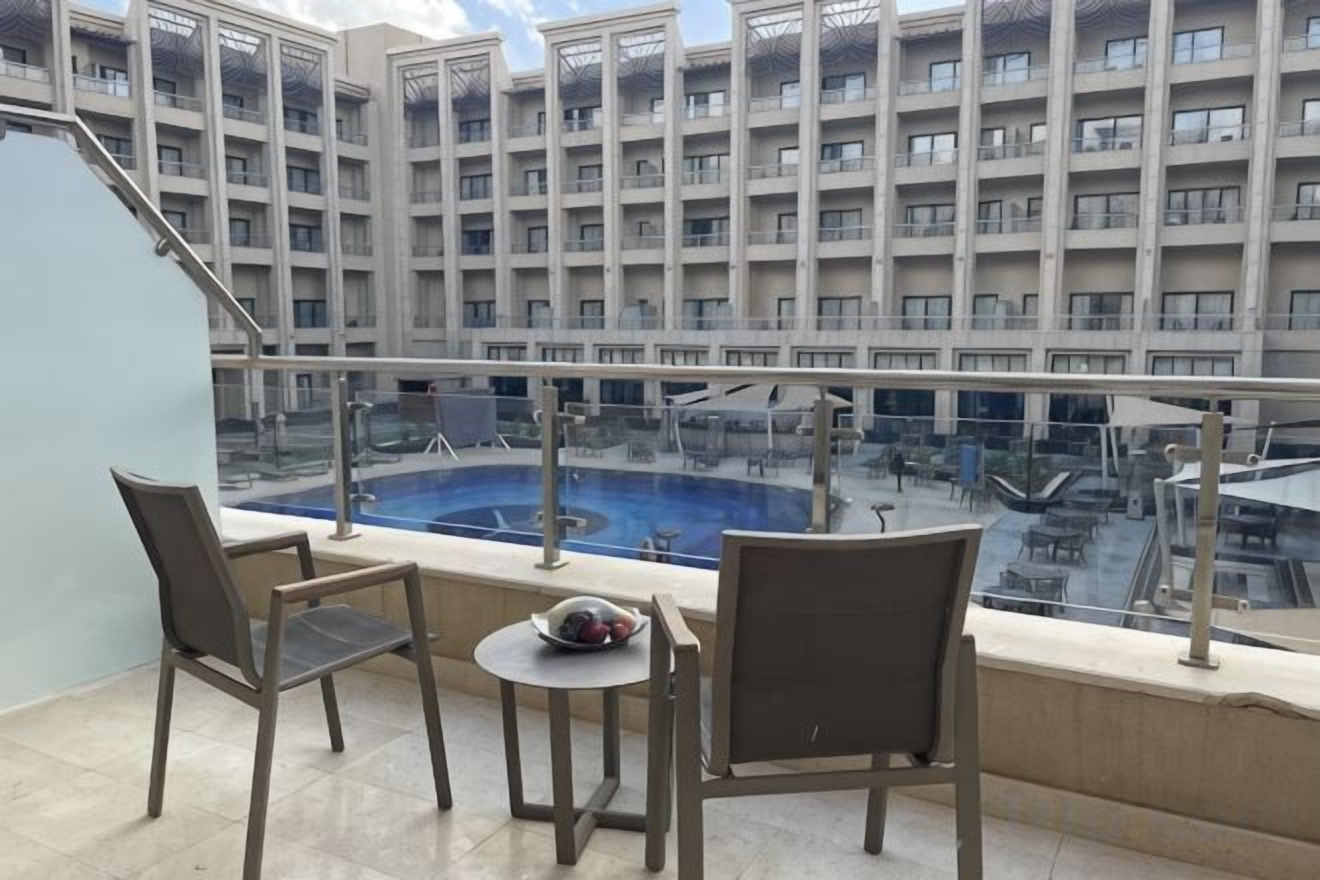 Un balcón con dos sillas y una mesita pequeña, con vistas a una piscina y un edificio de varios pisos.