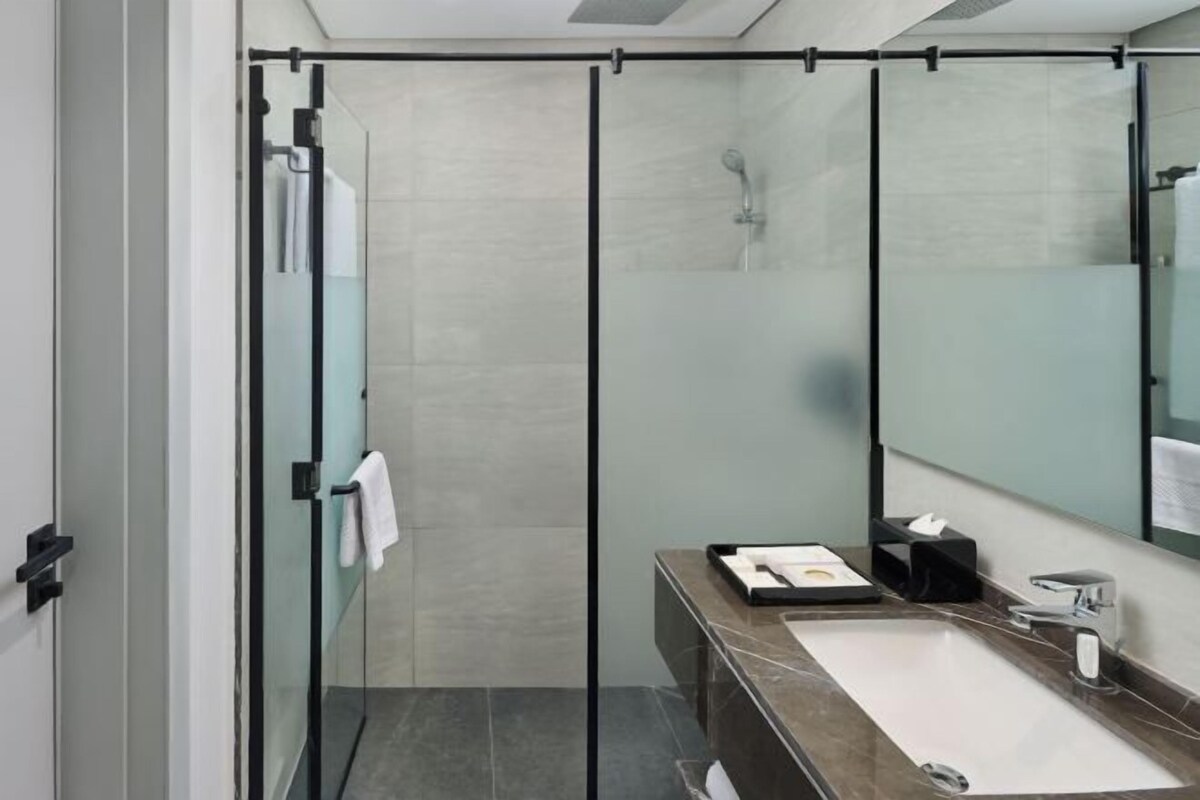 A modern bathroom with a glass shower enclosure, a sink with a mirror, and a towel rack.