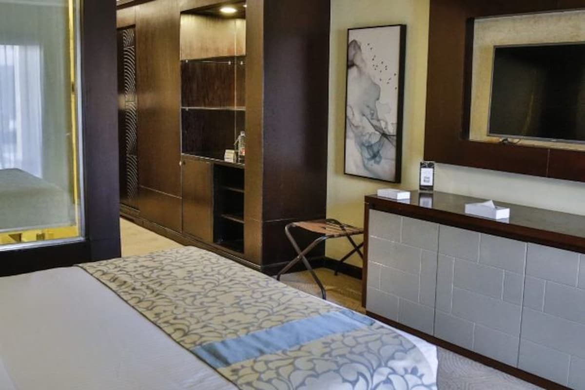 A hotel room with a bed, a desk, a chair, a TV, and a wardrobe.