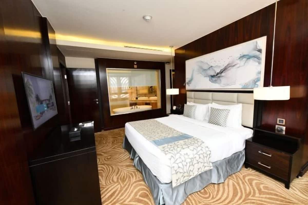 A hotel room with a large bed, a bathroom with a glass enclosure, a painting on the wall, and a wooden floor.