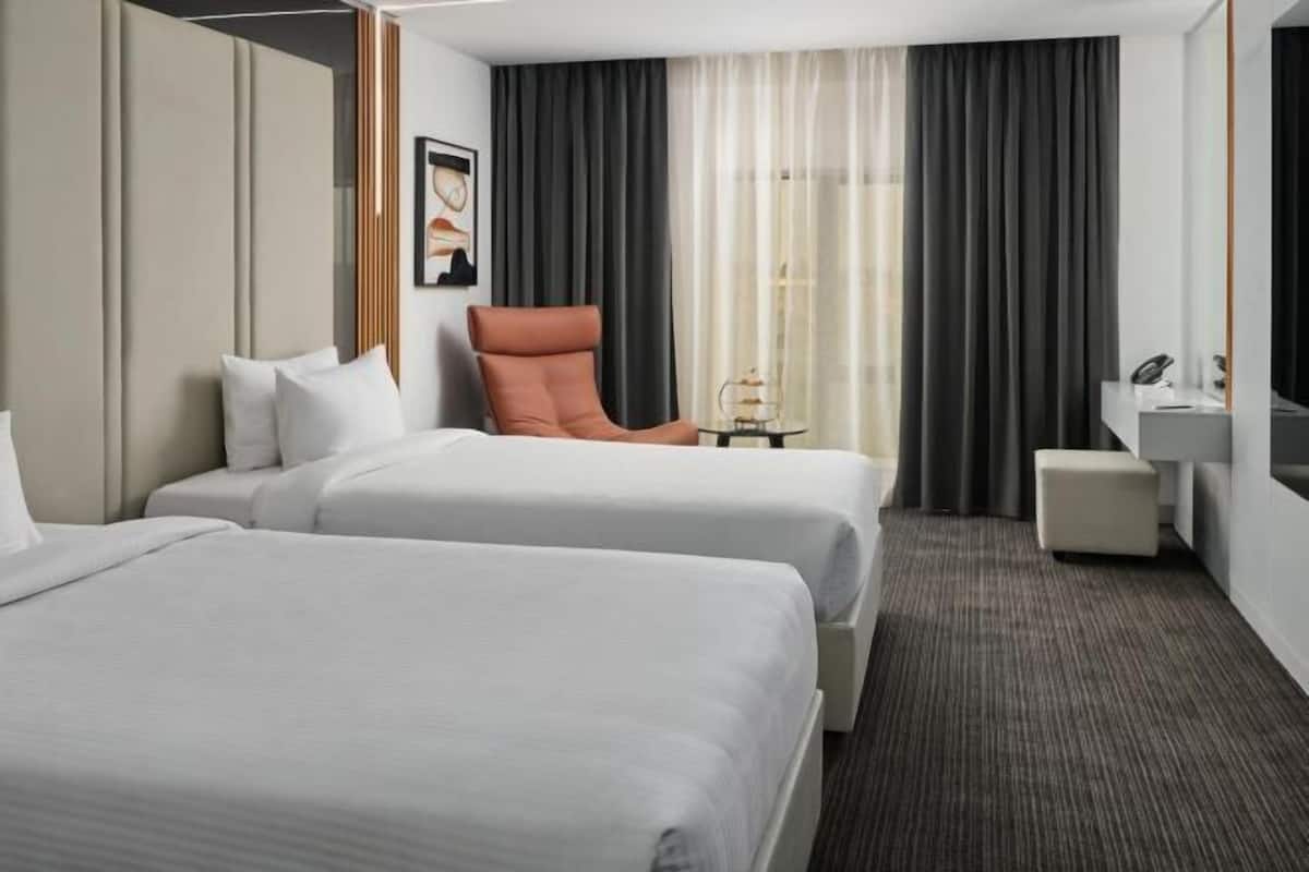 A hotel room with two beds, a seating area, a small table, and a mirror.