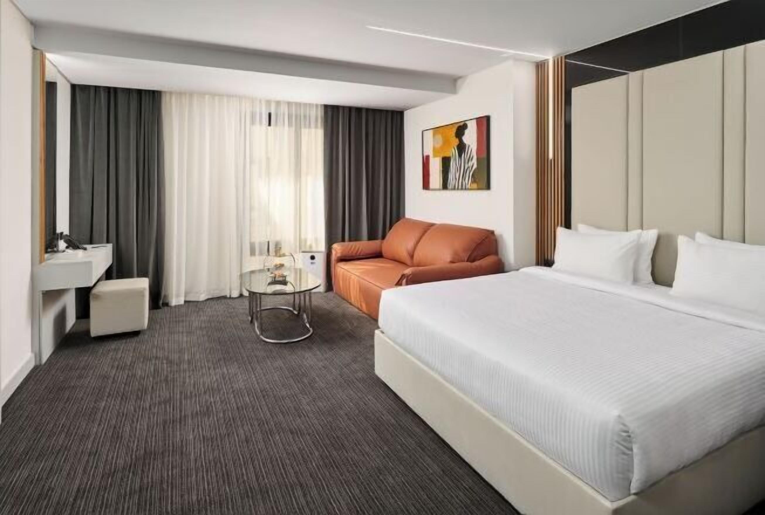 Una habitación de hotel con cama, sofá, una mesita, espejo y un cuadro en la pared.