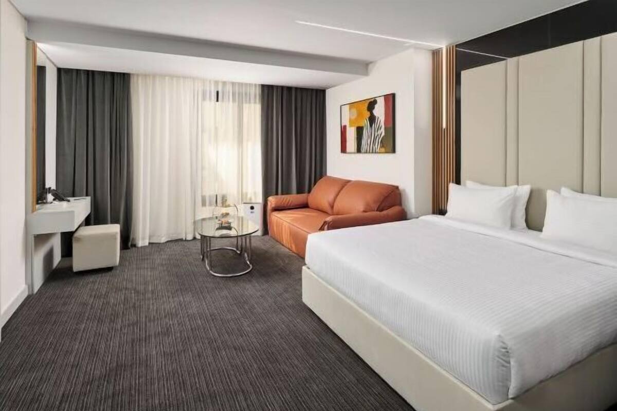 A hotel room with a bed, a sofa, a small table, a mirror, and a painting on the wall.