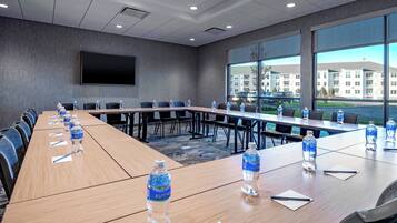 Un salón de conferencias con una larga mesa, botellas de agua y un amplio ventanal con vistas a edificios y automóviles.