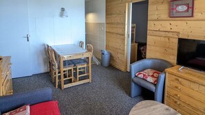 A compact room with a dining table, chairs, a sofa, a TV, and a wooden wall.