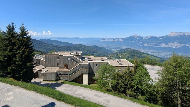A modern building with a unique architectural design, surrounded by lush greenery and mountains in the background.