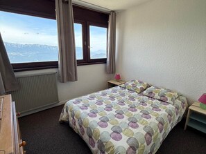 Una camera da letto con un letto, un comodino, una finestra con tende e vista sulle montagne.
