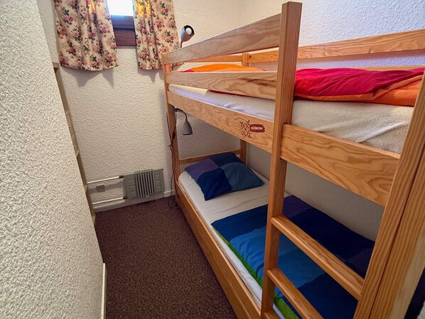 Habitación con literas, un radiador, una ventana con cortinas florales y una lámpara.