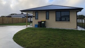 A small brick building with a metal roof, a fenced yard, and a grassy area in front.