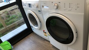 A front-loading washing machine with a control panel, a green basket, and a window view.