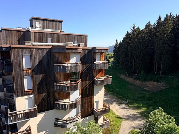 Ein mehrgeschossiges Gebäude mit Balkonen, einer flachen Dachterrasse und einem umgebenden Wald.
