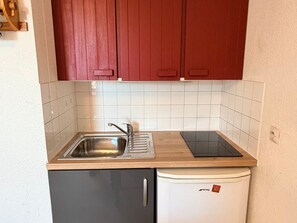 Eine kompakte Küchenzeile mit Spüle, kleinem Kühlschrank und Arbeitsplatte.