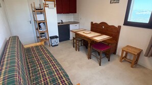 A compact room with a bed, a dining table with chairs, a small kitchen area, and a window.